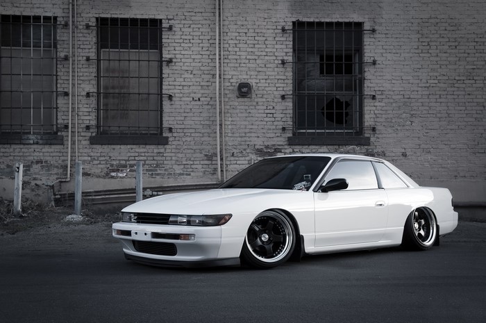 White Nissan Silvia S13 parked in front of a brick building