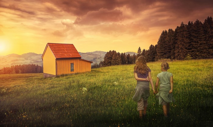 Two girls walking in a field at sunset near a house