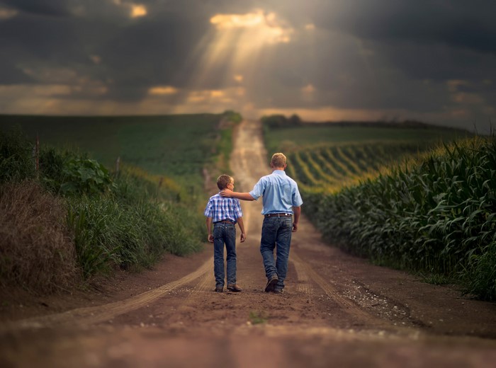 Two boys walking on a dirt road through fields