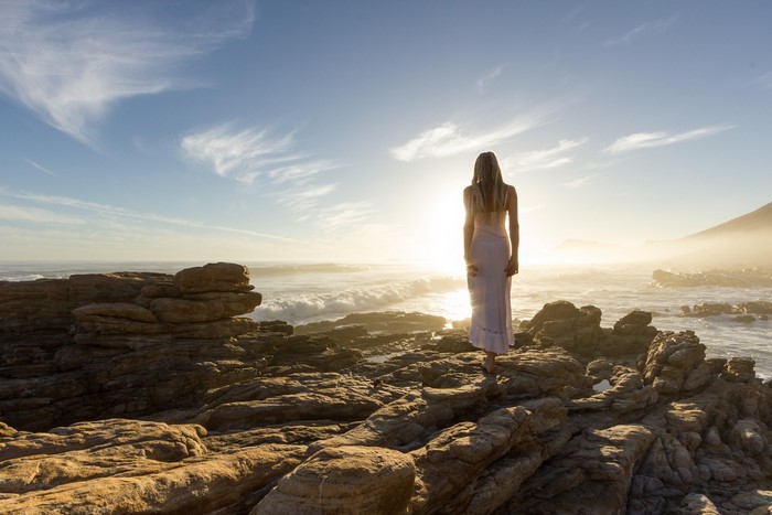 Woman in dress on rocky shore at sunset