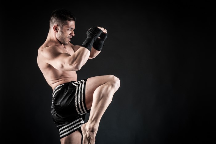 Man in boxing shorts performing a Muay Thai knee strike