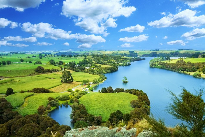 Green rolling hills and a blue river under a cloudy sky