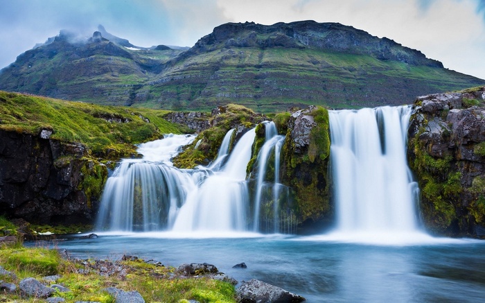 Waterfall cascading down mossy rocks with mountains in background