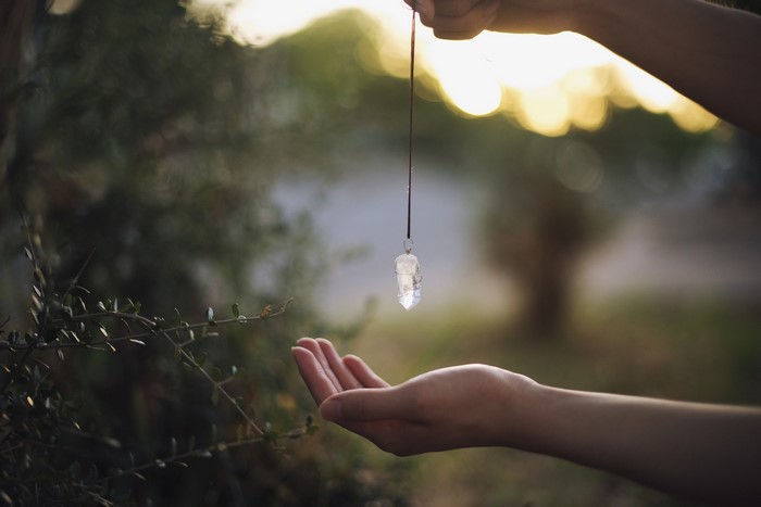 Hands holding a crystal pendulum over an open palm