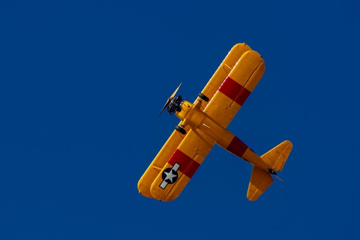 Yellow biplane with red stripes flying in blue sky