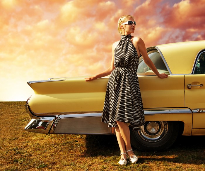 Woman in polka dot dress leaning on a yellow vintage car