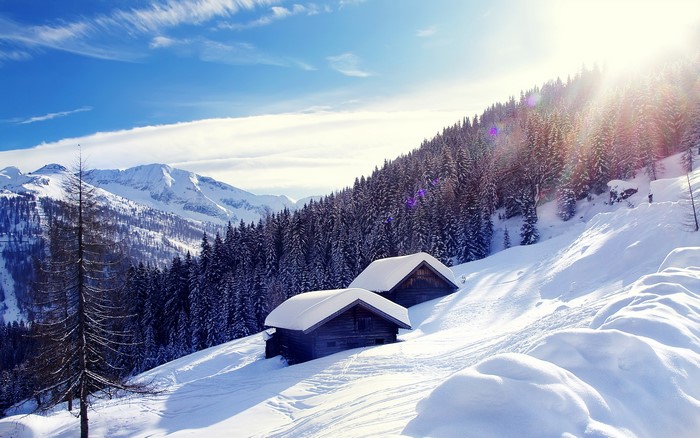 Two wooden cabins on a snowy mountain slope in the Alps
