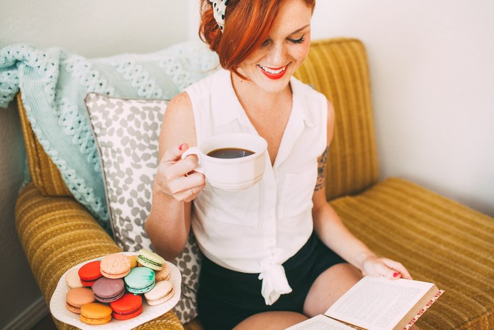 Redhead girl with macarons and coffee reading a book