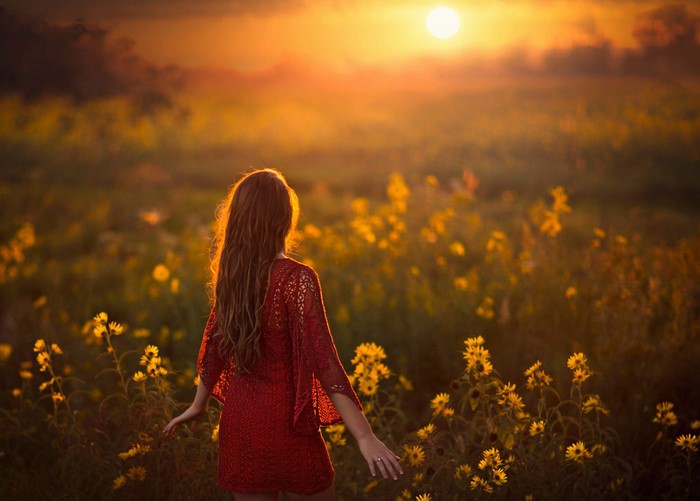 Woman in red dress in a field at sunset
