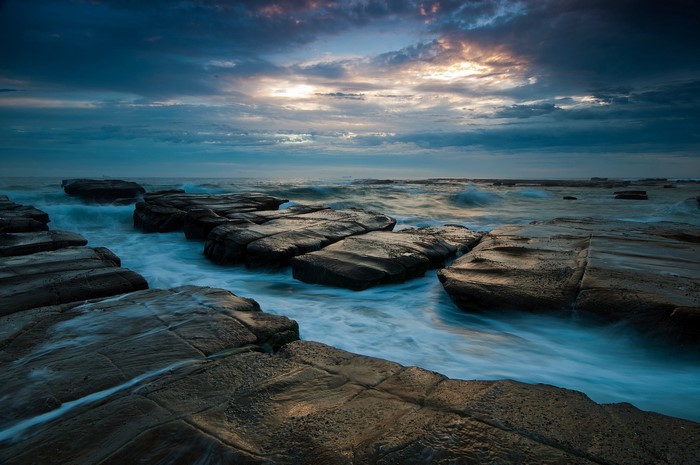 Ocean waves crashing on rocky shore at sunset