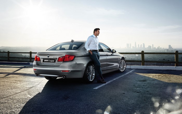 Man leaning on BMW 5 Series Sedan in parking lot
