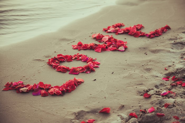 Love spelled with rose petals on a beach