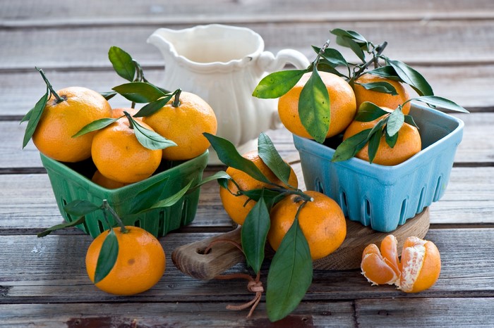 Tangerines with leaves in baskets and on a wooden table