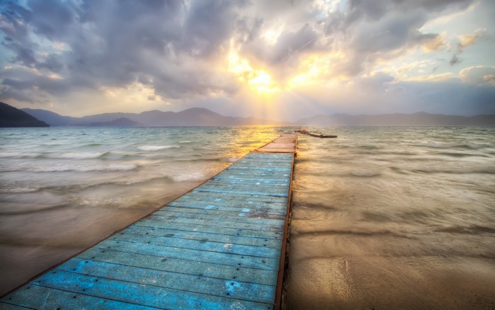 Wooden pier on a lake with mountains and sunbeams