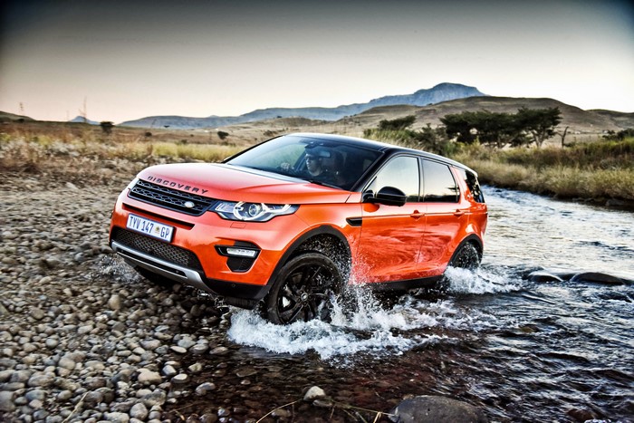 Orange Land Rover Discovery Sport driving through a rocky stream