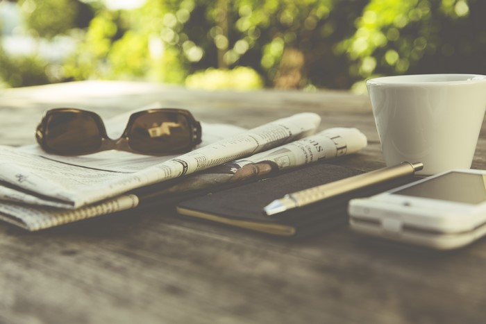 Sunglasses, Cup, Newspaper, Pen, and Phone on Table