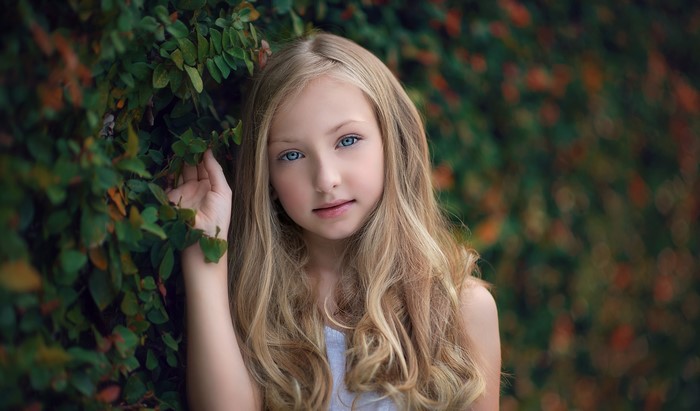 Blonde girl with blue eyes near green foliage