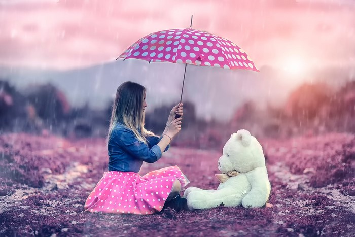 Girl holding umbrella over teddy bear in rain