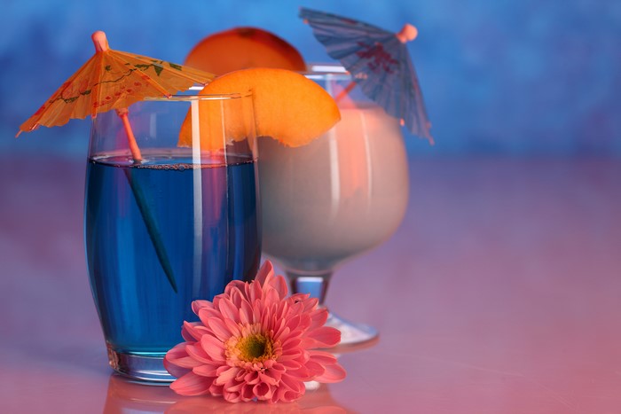 Two cocktails with fruit and flower garnish