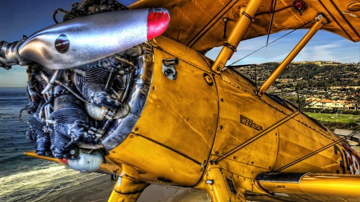 Yellow biplane engine and fuselage over ocean and town
