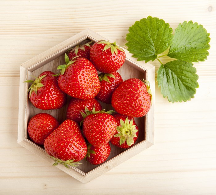 Strawberries in a hexagonal wooden tray with leaves