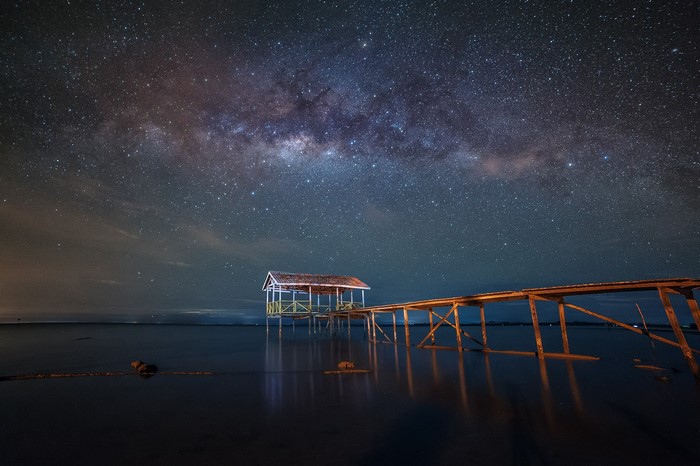 Milky Way over a wooden pier and hut on the water