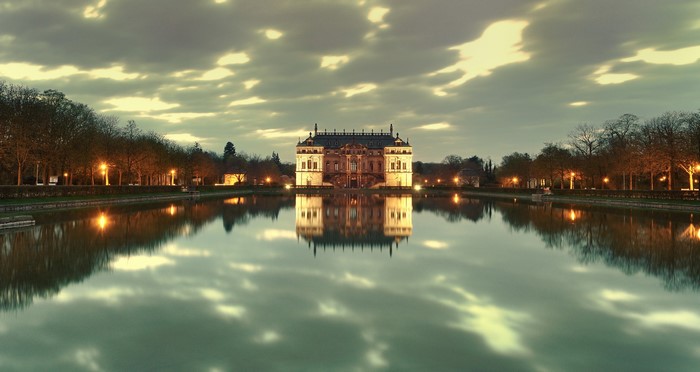 Palace reflected in a calm lake at dusk with illuminated trees