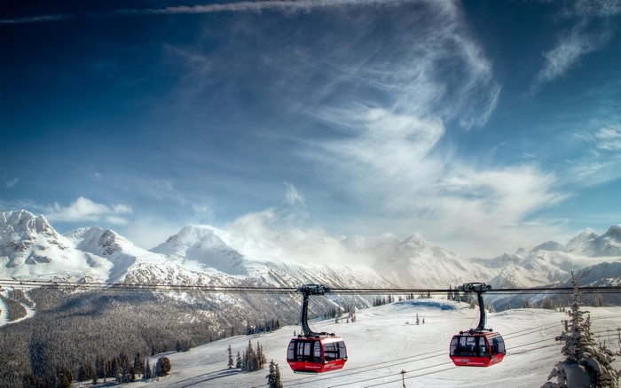 Two red gondolas ascend a mountain range on a sunny winter day.