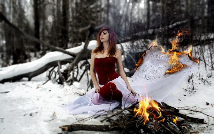 Woman in red corset and white dress by a fire in winter forest