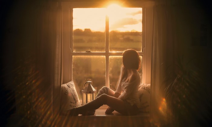 Woman sitting by the window at sunset