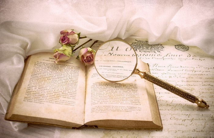Open book with magnifying glass and dried roses