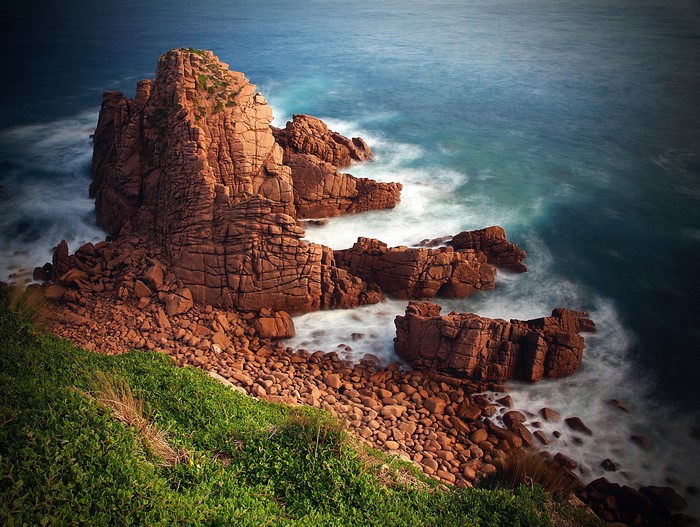 Rocky coast with crashing waves and green grass