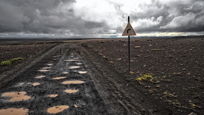 Muddy road with puddles and a curve sign