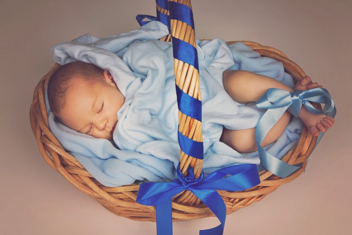 Infant sleeping in a wicker basket with blue ribbons