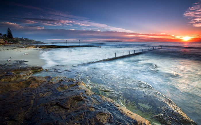 Ocean sunrise with rocky coast and swimming pool