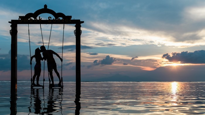 Couple kissing on a swing at sunset over the sea
