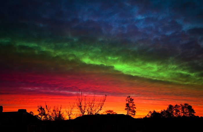 Rainbow sky over silhouetted trees at sunset
