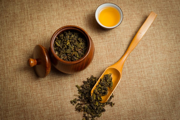 Tea leaves in a wooden container and spoon with a cup of tea