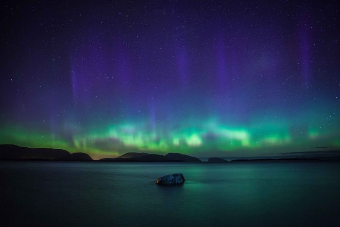 Aurora Borealis over a calm body of water with mountains