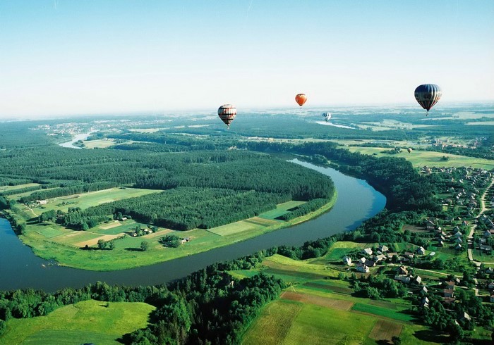 Hot air balloons over a river and forest in Lithuania