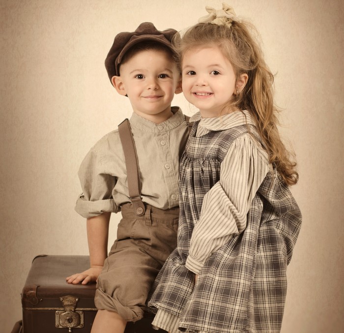 Children in vintage clothing posing on a suitcase