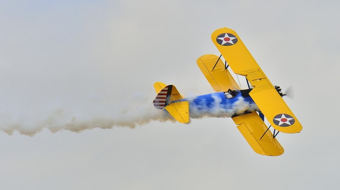 Yellow biplane performing aerobatics with smoke