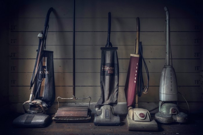 Four vintage Hoover vacuum cleaners lined up against a wall
