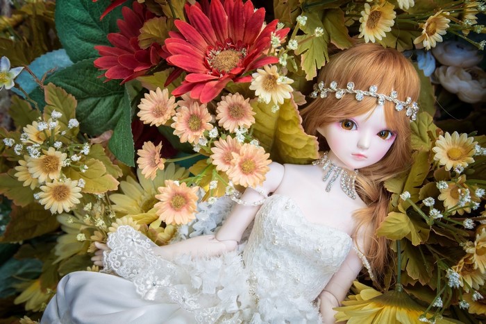 Doll wearing a white dress and jewelry among flowers