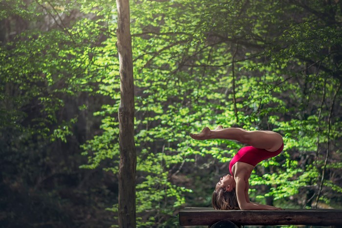 Woman performing yoga pose on a wooden bench in a forest