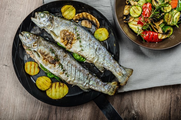 Two whole grilled trout with grilled vegetables and potatoes