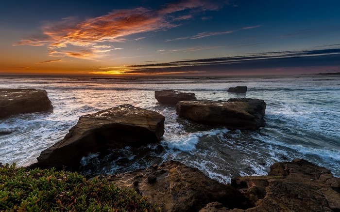 Sunset over the ocean with rocks and waves