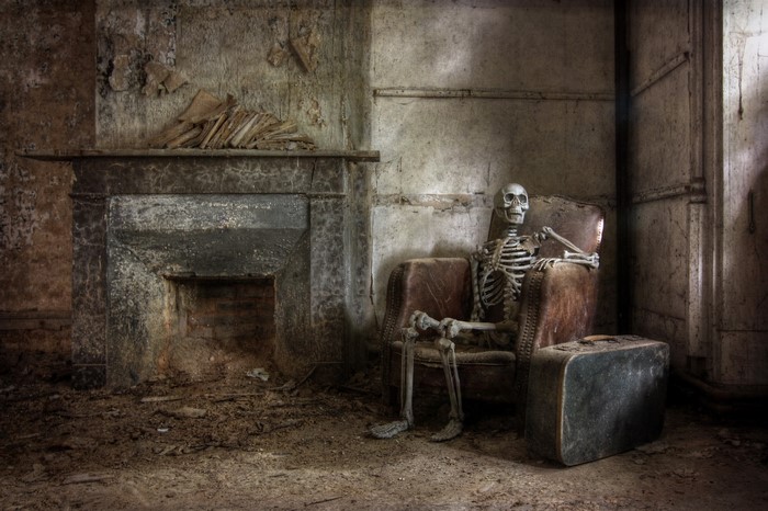 Skeleton sitting in an armchair in an abandoned room