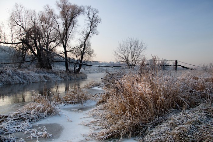 Winter river with frost-covered grass and a wooden bridge