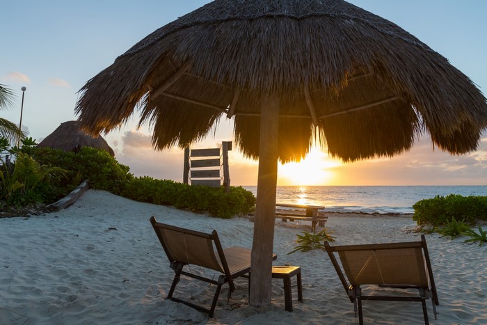 Beach with thatched umbrella and sun loungers at sunset